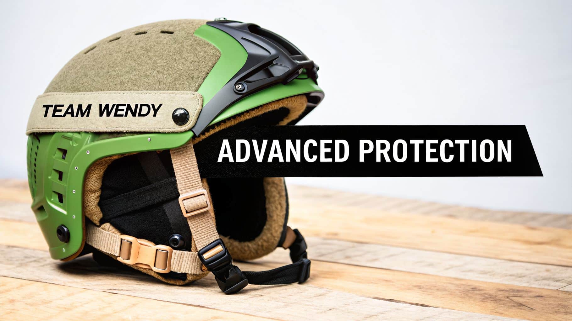 A green and tan Team Wendy tactical helmet with 'Advanced Protection' text rests on a wooden surface.