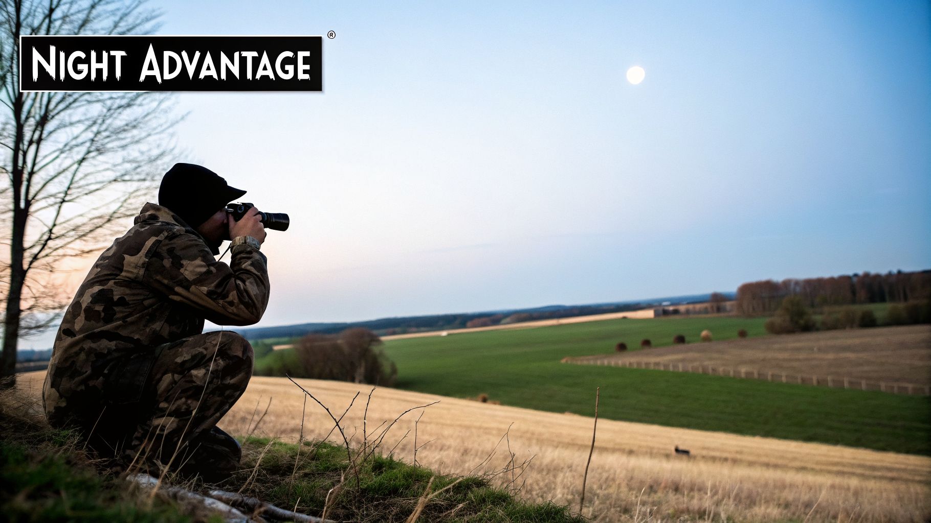 A person in camouflage gear crouches on a hill, taking photos of a moonlit field at dusk.