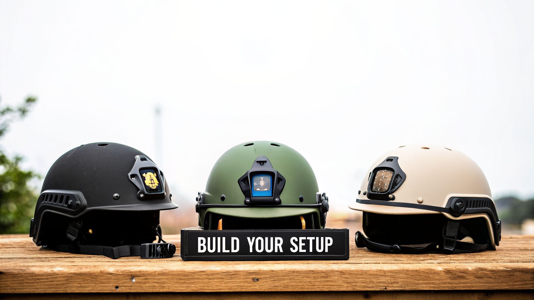 Three tactical helmets in black, olive green, and tan on a wooden table, with a 'BUILD YOUR SETUP' sign.