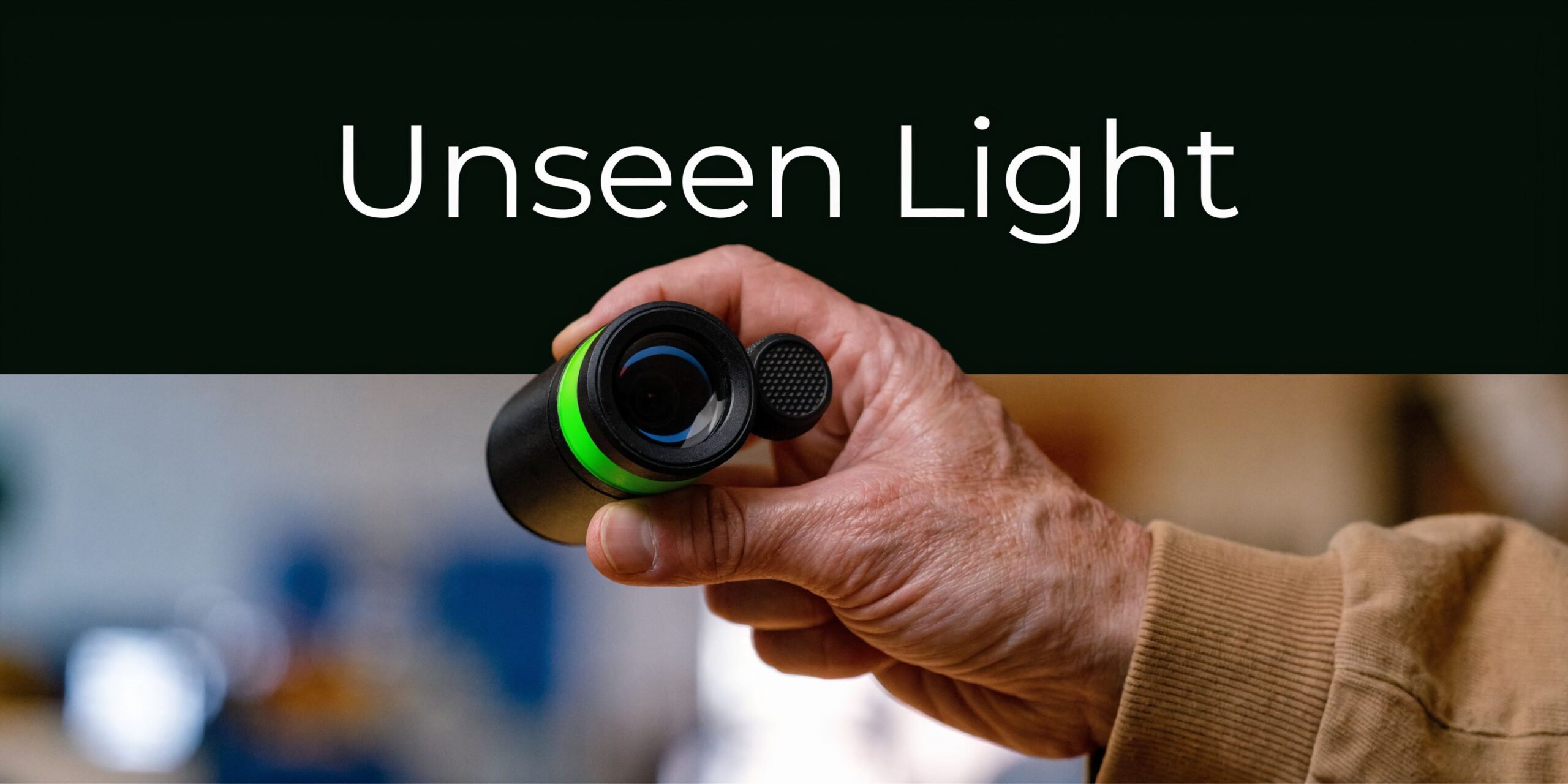 A close-up of an elderly person holding a small black monocular device with a bright green ring.